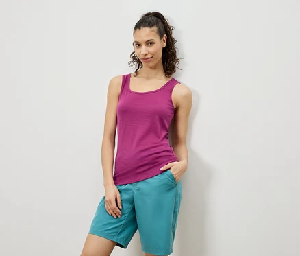 Frau posiert in einem pinken Tanktop und türkisfarbenen Shorts vor einer weißen Wand.