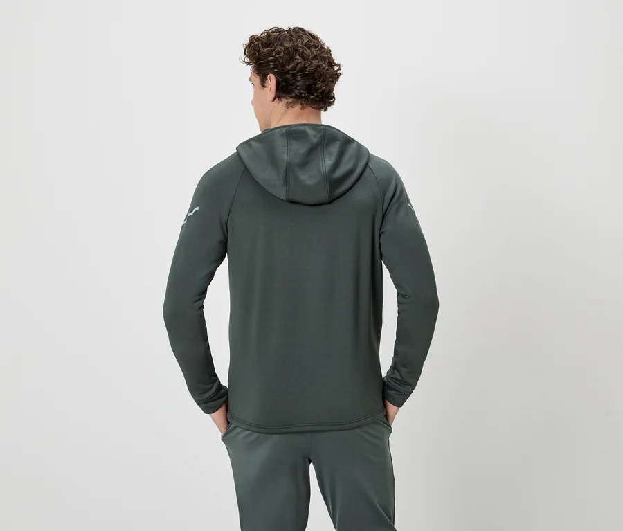 Ein Mann mit lockigem Haar steht mit dem Rücken zur Kamera und trägt einen dunkelgrünen Hoodie und eine Jogginghose.