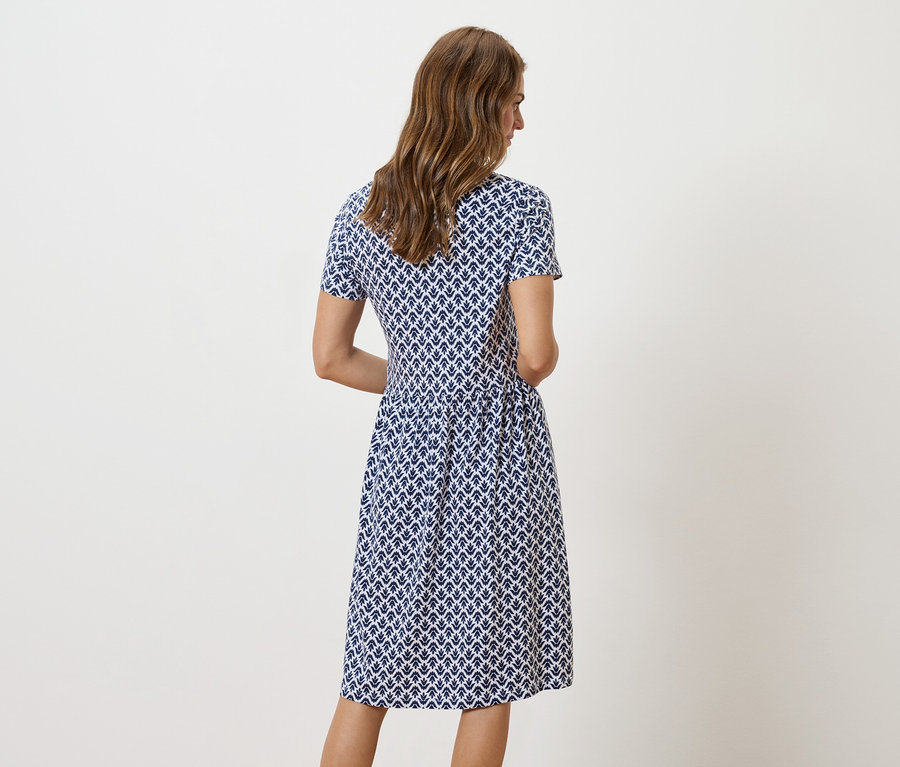 Eine Frau steht mit dem Rücken zur Kamera und trägt ein blau-weiß gemustertes Kleid.