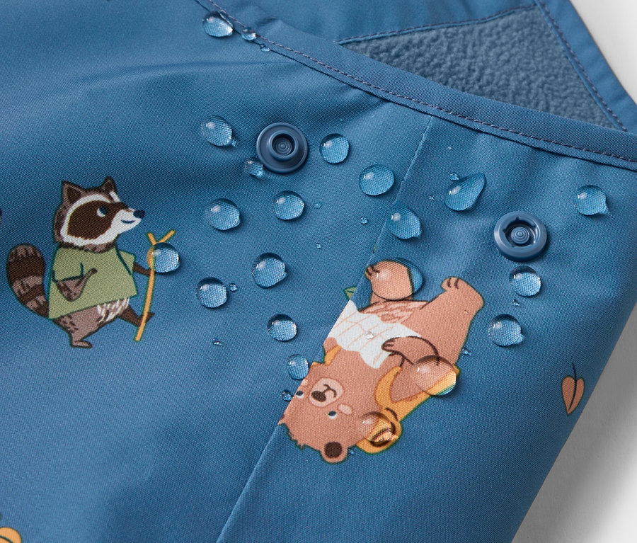 Nahaufnahme eines blauen Stoffes mit Knopfverschlüssen, Wassertropfen und Bären- und Waschbär-Motiven.