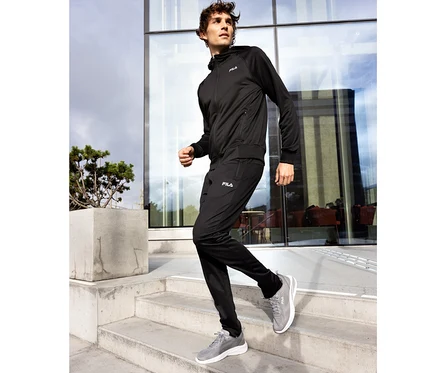 Mann in schwarzer FILA Herren-Funktions-Sweatjacke und schwarzer Trainingshose läuft eine Betontreppe hinunter.