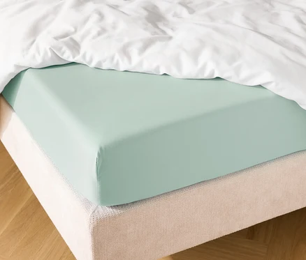 Nahaufnahme eines Bettes mit hellblauem Spannbettlaken und einer weißen Bettdecke.
