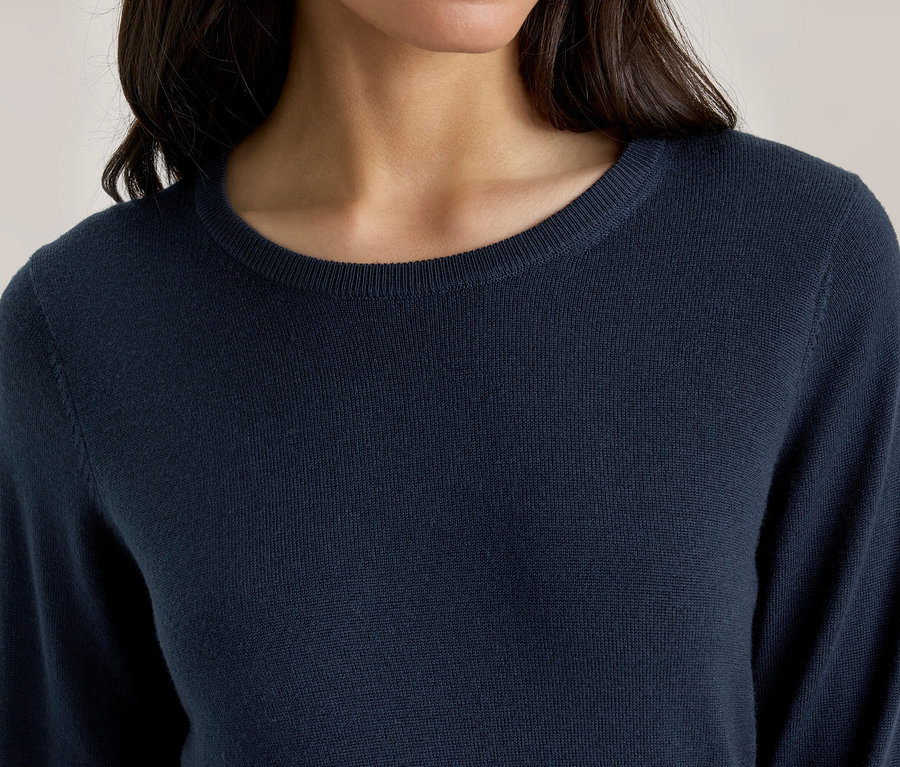 Nahaufnahme einer Person in einem dunkelblauen, langärmeligen Pullover mit Rundhalsausschnitt.