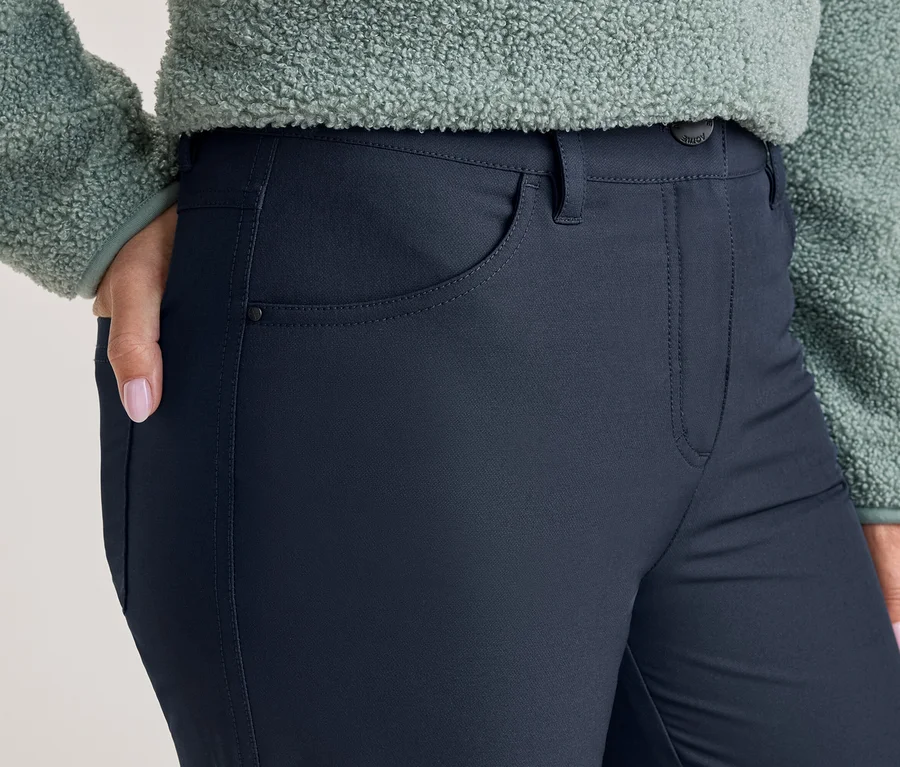 Person trägt dunkelblaue Hose und hellgrünes Fleece-Oberteil. Die rechte Hand mit rosa Nagellack steckt in der Hosentasche.