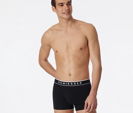 Oben ohne Mann trägt schwarze SCHIESSER Shorts, blickt nach rechts und lächelt.
