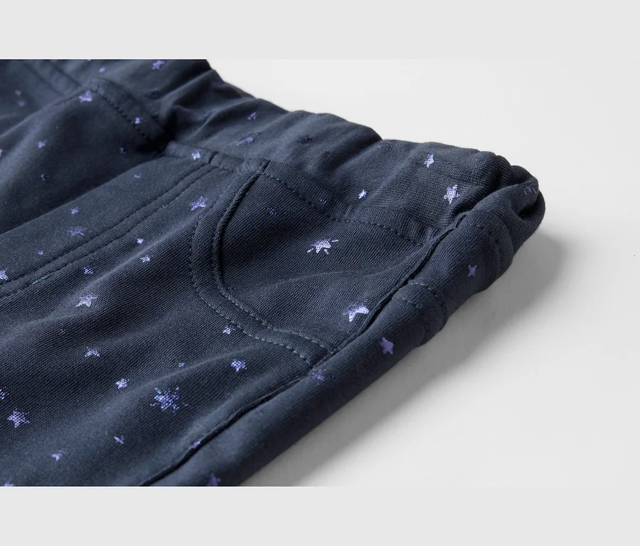 Nahaufnahme eines dunkelblauen Stoffes mit kleinen, hellvioletten Stern- und Halbmondmustern, der einen elastischen Bund und eine Taschendetail zeigt.