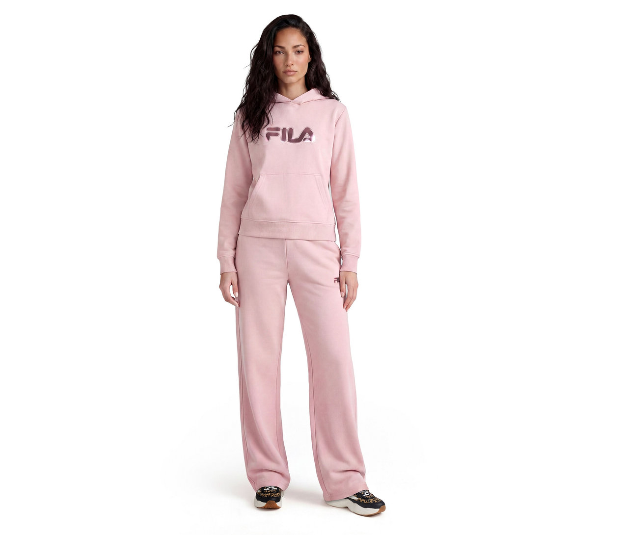Frau steht in einem rosa Fila Hoodie mit Bauchtasche und passender weiter Jogginghose, kombiniert mit dunklen Turnschuhen.