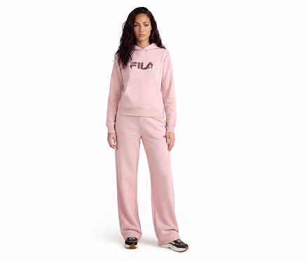Frau steht in einem rosa Fila Hoodie mit Bauchtasche und passender weiter Jogginghose, kombiniert mit dunklen Turnschuhen.