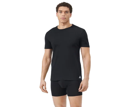 Mann mit kurzen Locken trägt ein schlichtes schwarzes T-Shirt mit weißem Logo an der linken Hüfte und schwarze Boxershorts vor weißem Hintergrund.
