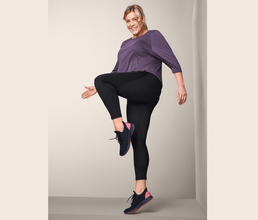 Frau mit blonden Haaren hebt ihr Knie in schwarzen Sporttights.