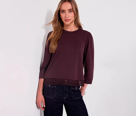 Eine Frau trägt ein rotes Street One 3/4-Jerseyshirt mit Spitzenbesatz am Saum und dunkle Jeans.
