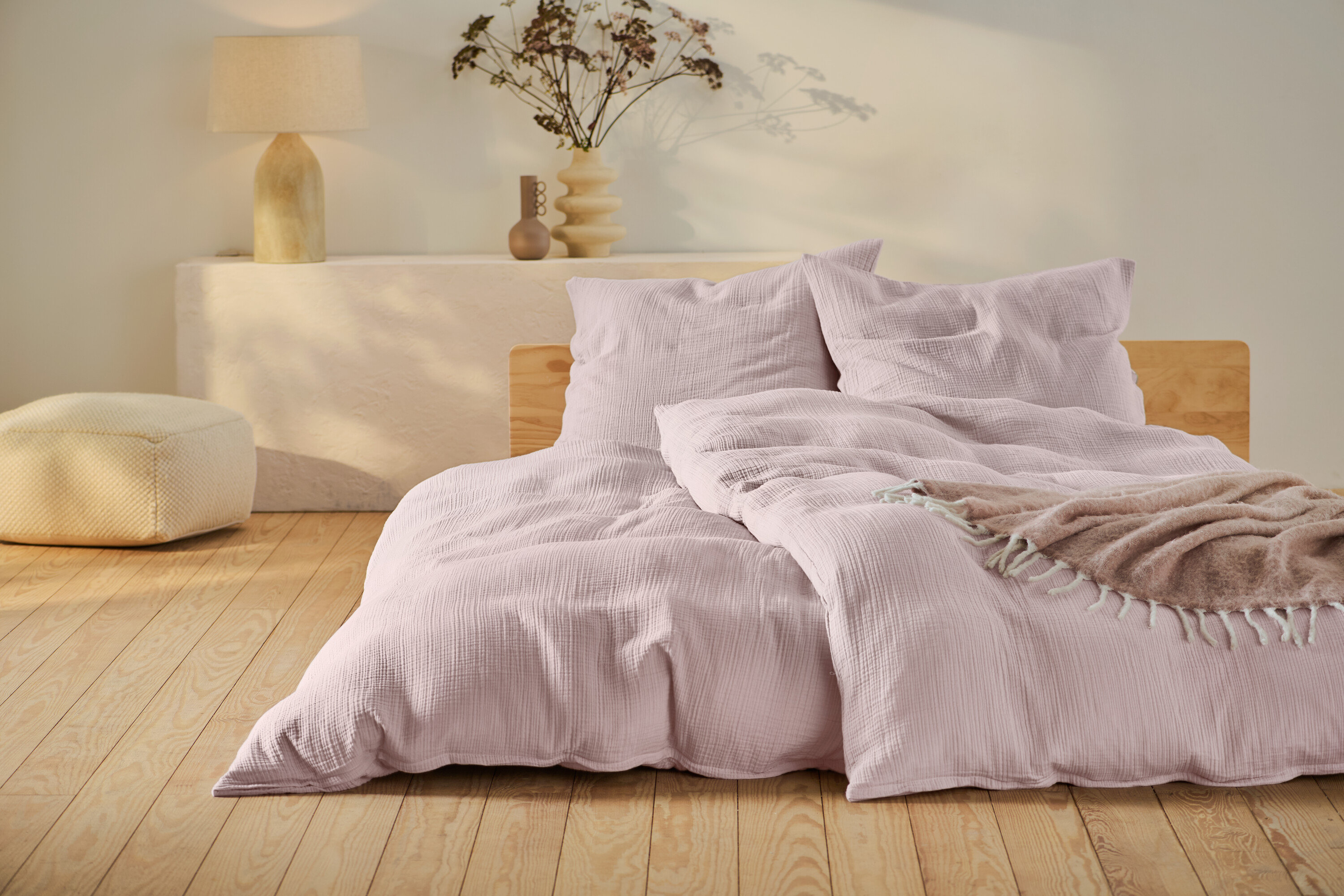 Rosafarbene Musselin-Bettwäsche in Normalgröße und Übergröße auf einem Bett mit Holzrahmen.