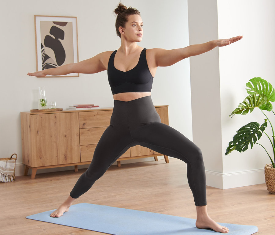 Frau in Sportkleidung macht Yoga auf einer blauen Matte. Sie trägt eine 7/8-Premium-Sporttight.