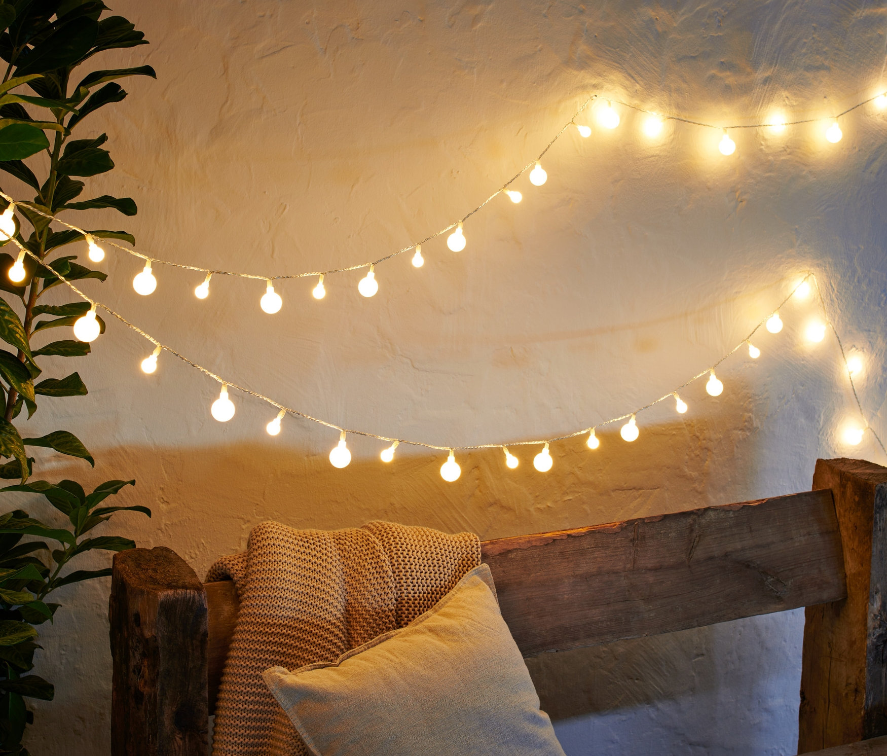 Zwei LED-Outdoor-Lichterketten hängen über einer Holzbank mit Kissen und Decke.