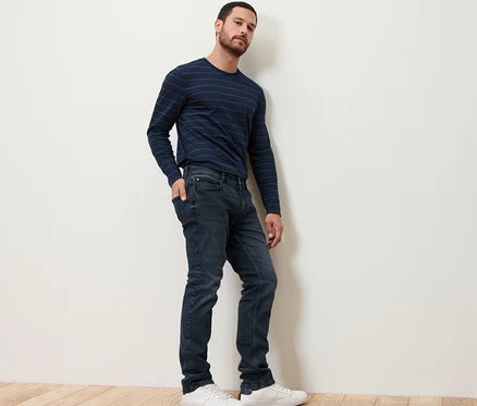 Mann posiert in Jeans und gestreiftem Shirt.