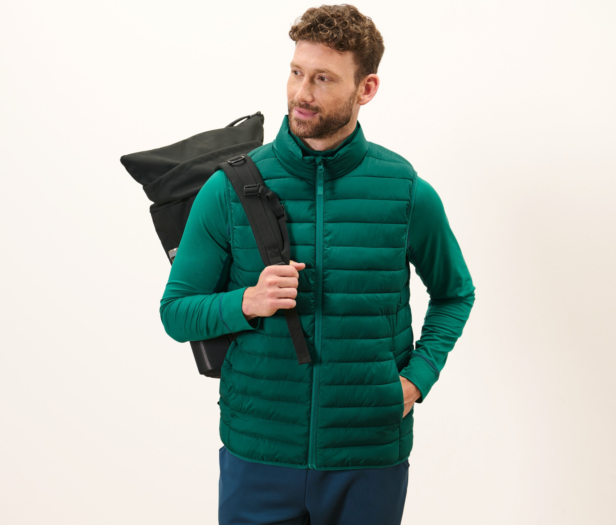 Mann trägt eine grüne verstaubare Steppweste und einen schwarzen Rucksack.