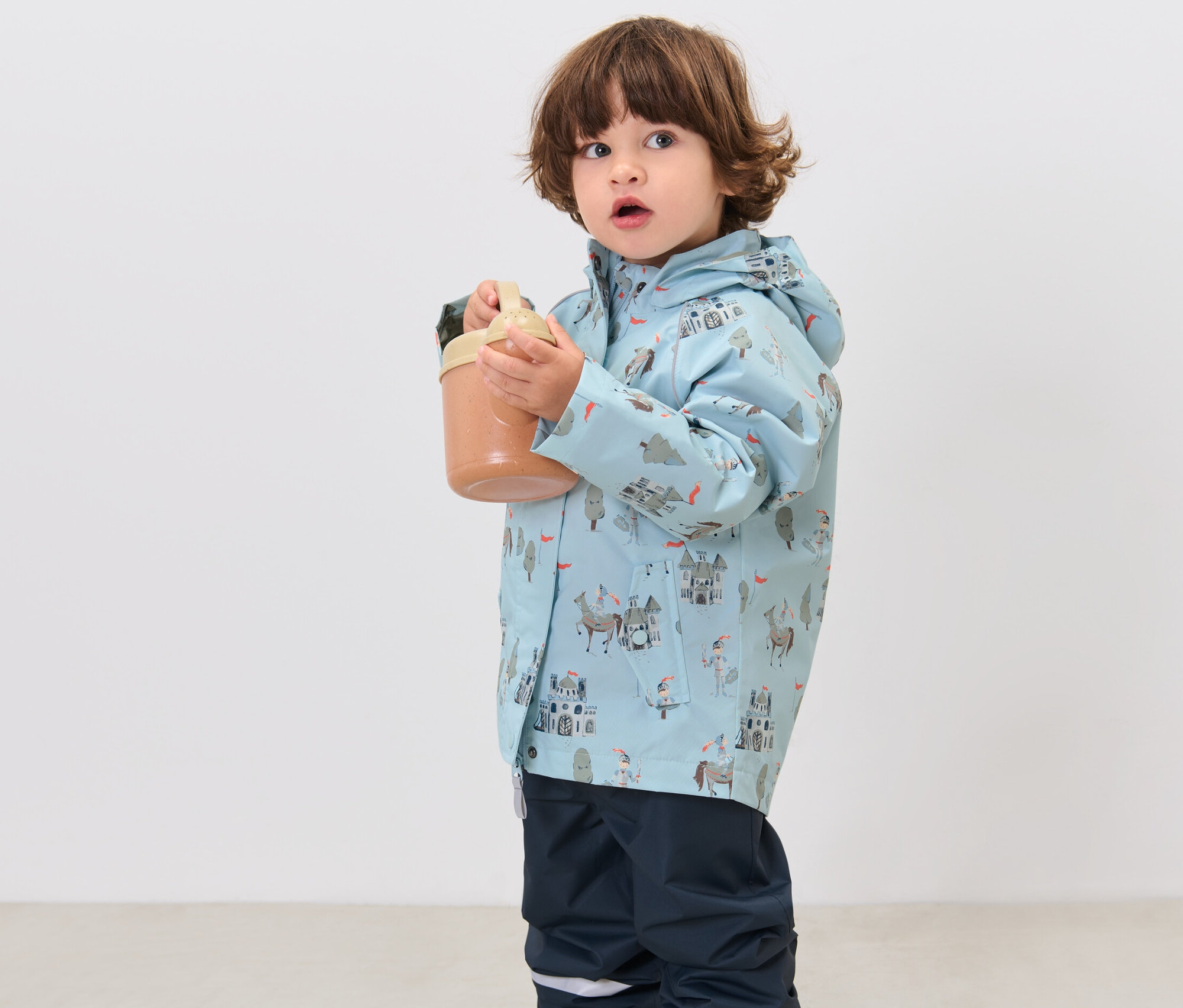 Junge hält einen Becher und trägt eine Kinder-Regenjacke, Ritter.