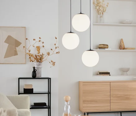Wohnzimmer mit rundem Couchtisch, Sideboard »Finnsbo« mit Lamellenoptik und Design-Konsole mit Glasfächern. Darüber hängt eine 3-flammige Hängeleuchte mit Glaskugeln.