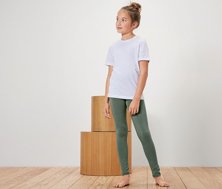 Ein Mädchen in einem weißen T-Shirt und grünen Leggings steht neben Holzzylindern.