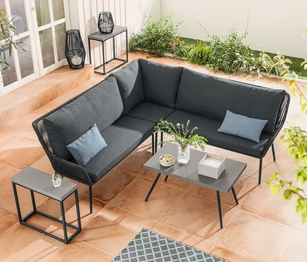 Eine Lounge-Ecke mit Textilgeflecht steht neben einem Couchtisch mit Polyzement-Tischplatte. Ein Konsolentisch-Set mit Polyzement-Tischplatte steht neben einer Solar-Laterne mit Textilband.