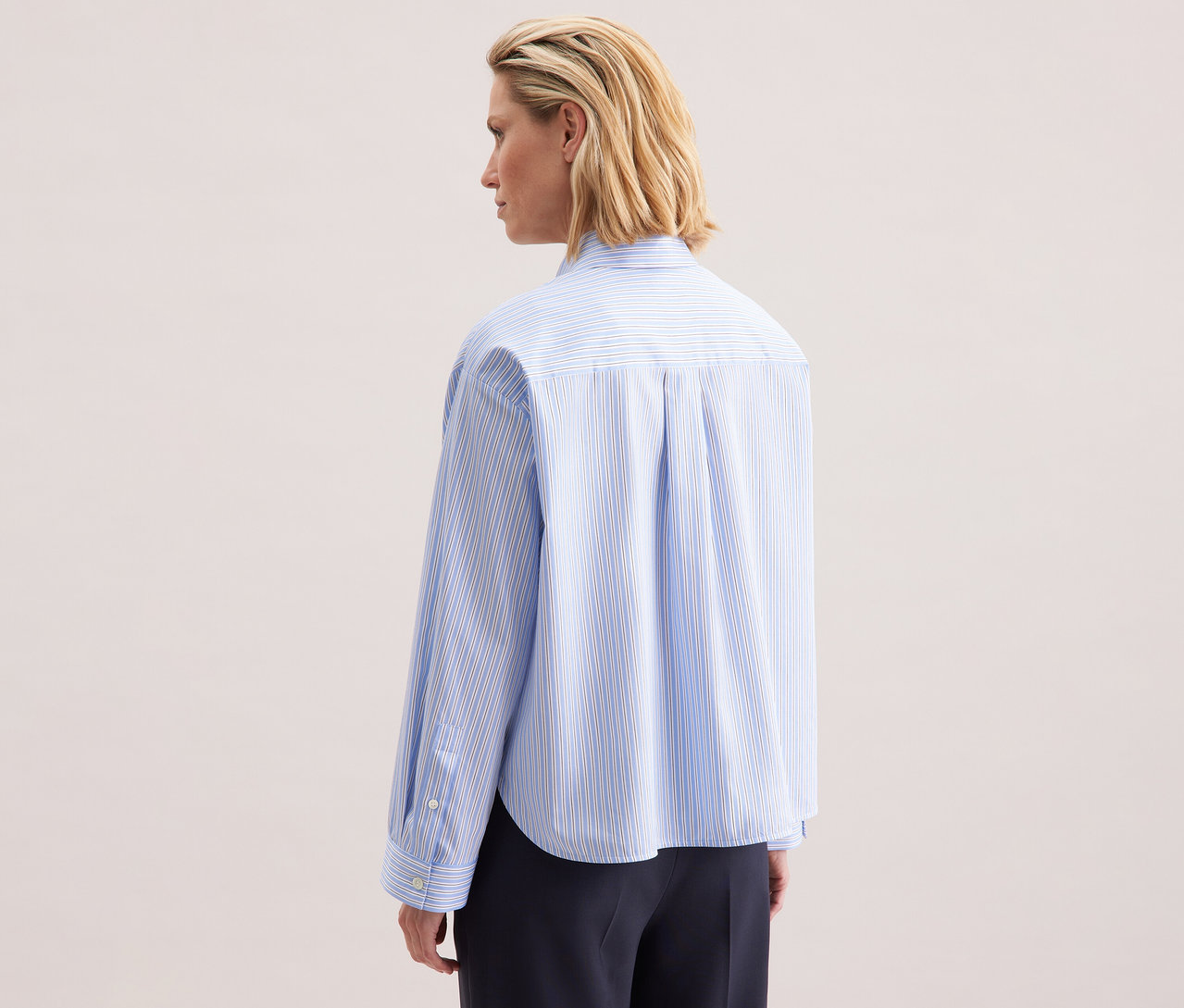 Rückansicht einer blonden Frau, die eine blau-weiß gestreifte Seidensticker Oversize-Hemdbluse trägt.