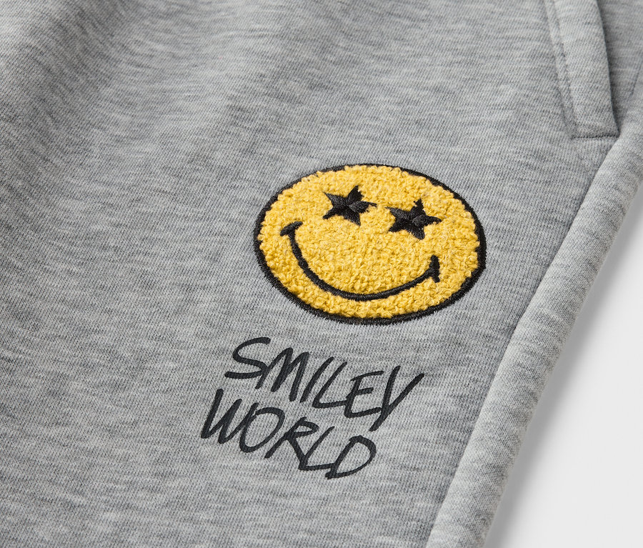 Detail einer grauen Kinder-Jogginghose SMILEYWORLD® mit gelbem Smiley-Aufnäher.