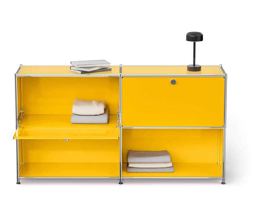 Gelber Schrank mit offenem Fach, in dem gefaltete Kleidung liegt, oben liegen Bücher und eine Lampe.