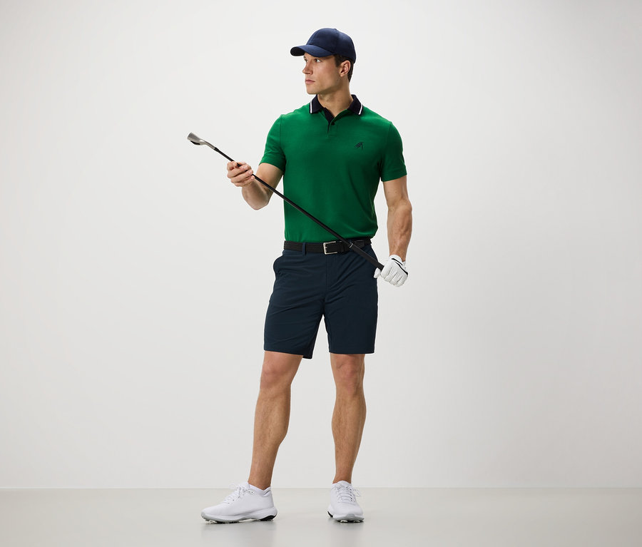 Mann hält Golfschläger und trägt Funktionsshorts.