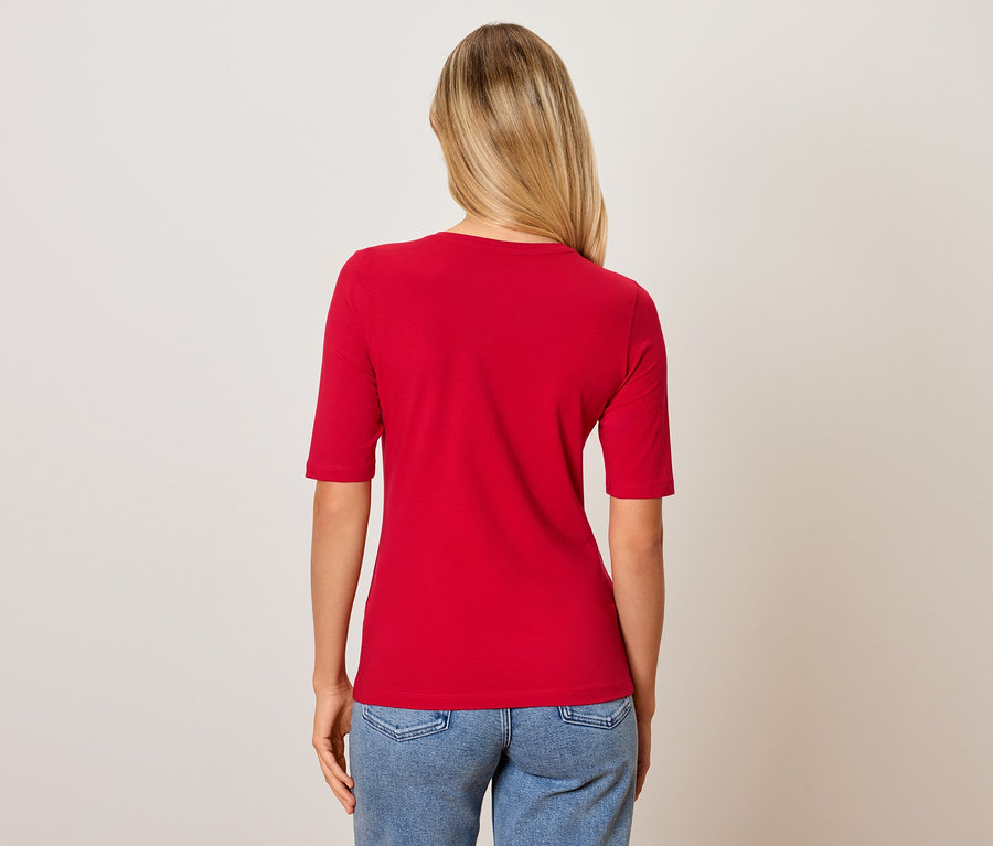 Rückansicht einer Frau mit blonden Haaren, die ein rotes T-Shirt und blaue Jeans trägt.