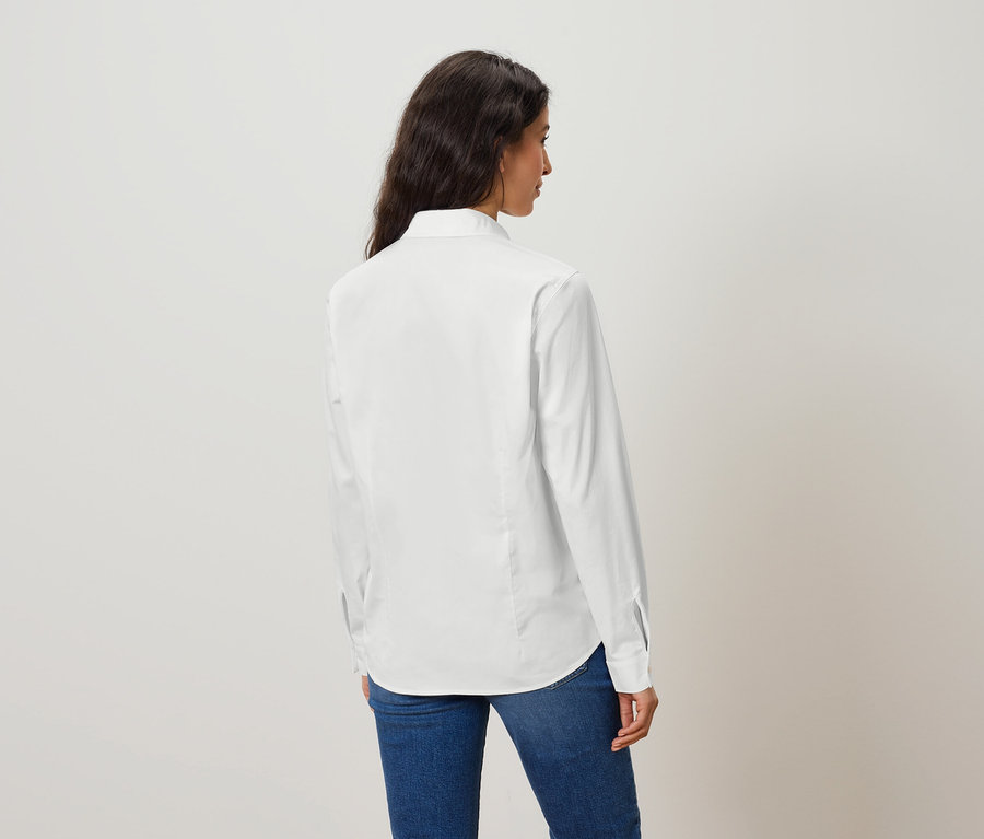 Frau trägt ein weißes Langarmhemd und Jeans, mit dem Rücken zur Kamera.