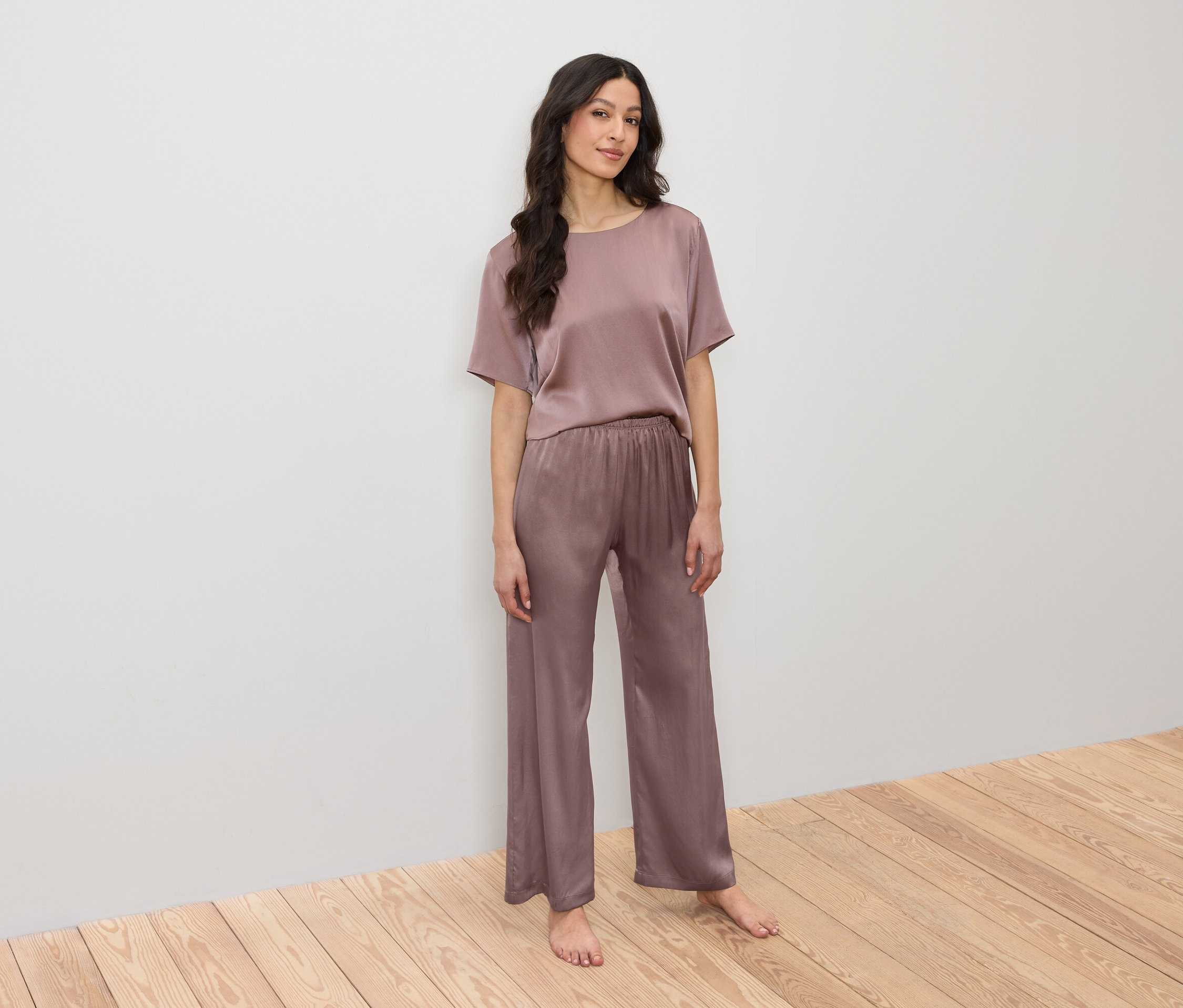 Frau posiert in einem rosafarbenen Satin-Pyjama, bestehend aus einem T-Shirt und einer Hose.