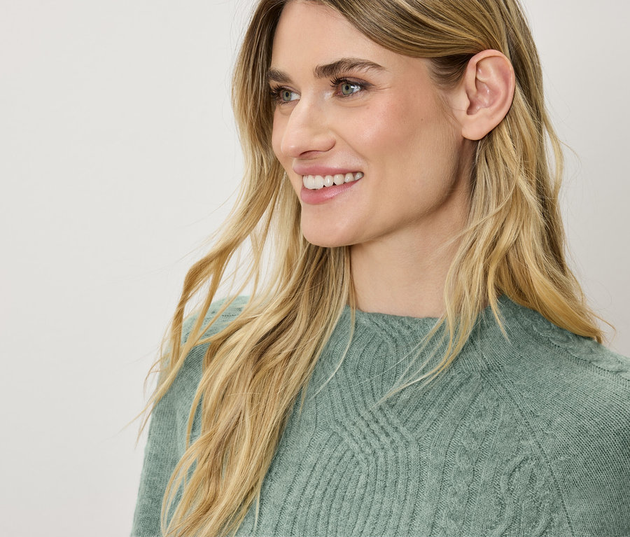 Profilansicht einer lächelnden Frau mit blonden Haaren in einem grünen Pullover.