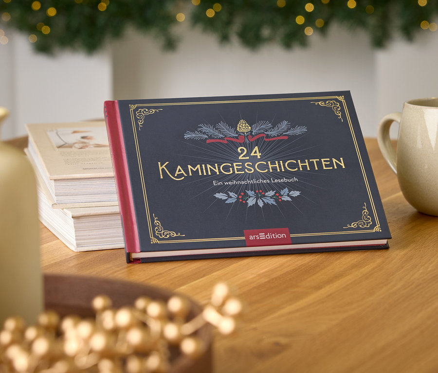Buch "24 Kamingeschichten" auf einem Holztisch neben einer Tasse und einer Vase, im Hintergrund ein Weihnachtsbaum.