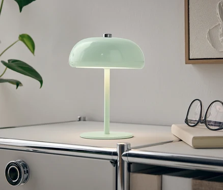 Eine grüne Lampe steht auf einem weißen Nachttisch neben einer Pflanze und einer Brille.
