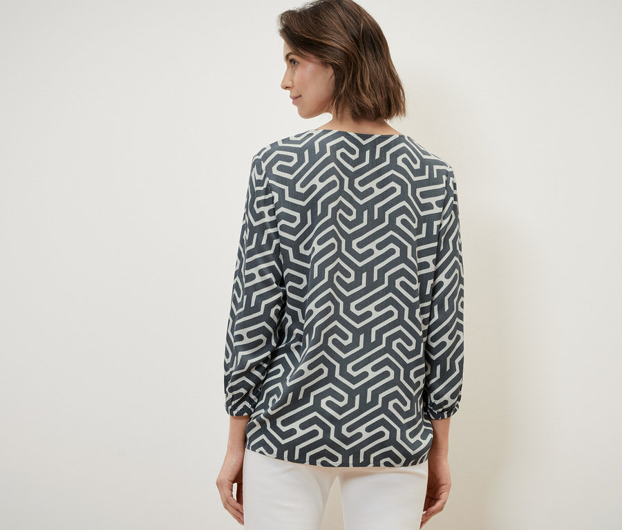 Eine Frau mit dem Rücken zur Kamera trägt eine Bluse in Crinkle-Optik und eine weiße Hose.