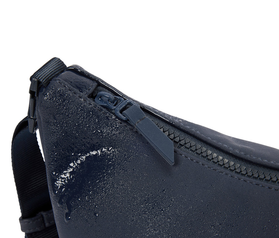 Nahaufnahme einer dunkelblauen Bauchtasche mit Reißverschluss und Wassertropfen.