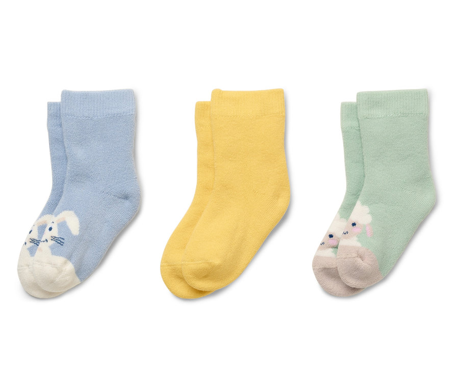 Drei Paar Kindersocken, hellblau mit Hasen, gelb und hellgrün mit Schaf, liegen nebeneinander.