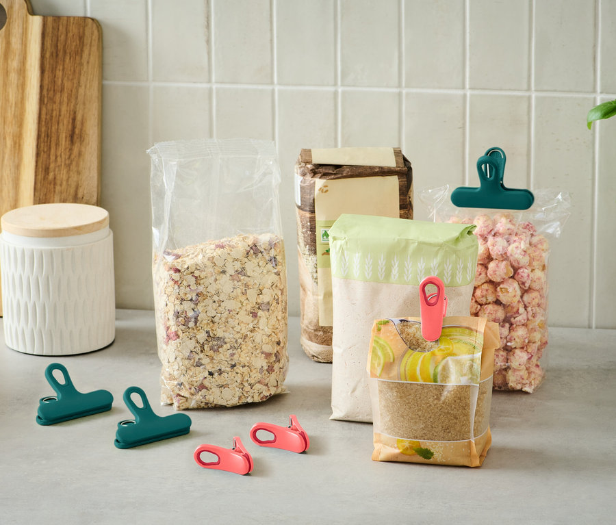 Verschiedene offene Lebensmittelverpackungen stehen auf einer Küchentheke, einige mit Klemmen in Grün und Pink verschlossen.