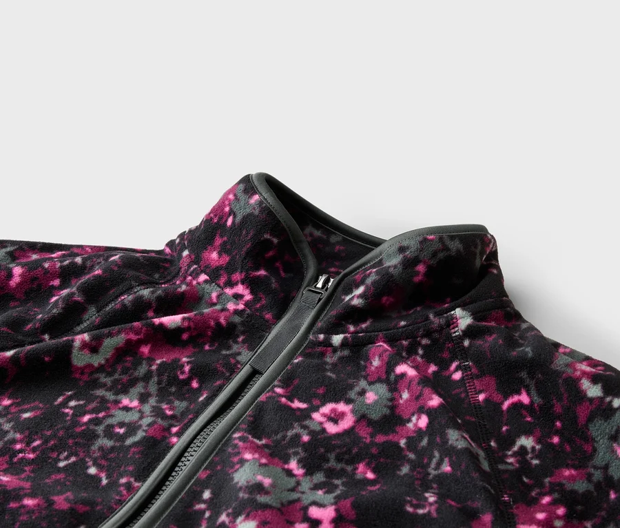 Nahaufnahme einer Fleecejacke mit Reißverschluss und abstraktem Blumenmuster in Pink und Grau.
