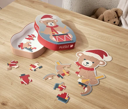 Ein Bär-Puzzle mit Weihnachtsmütze liegt zerlegt auf einem Tisch, daneben die Schachtel.
