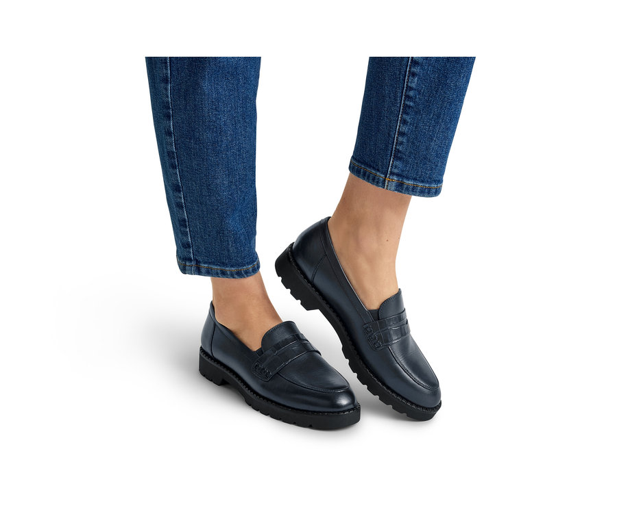 Beine und Füße einer Person in blauen Jeans und dunkelblauen Loafern mit dicken schwarzen Sohlen.