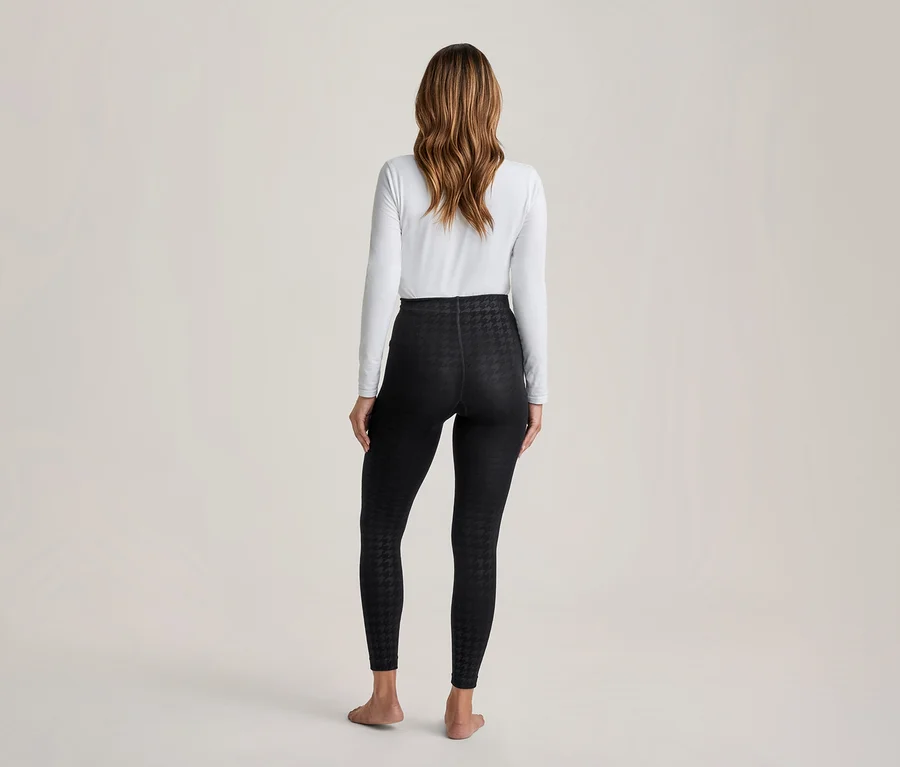 Frau steht mit dem Rücken zur Kamera, trägt weißes Langarmshirt und schwarze Leggings mit Hahnentrittmuster, barfuß.