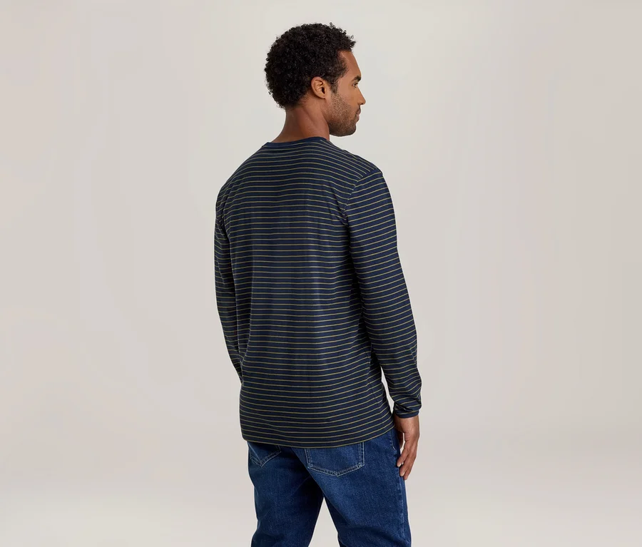 Mann mit dunklem Lockenhaar, von hinten und leicht nach rechts gedreht, trägt ein dunkelblaues Langarmshirt mit dünnen hellen Querstreifen und blaue Jeans.