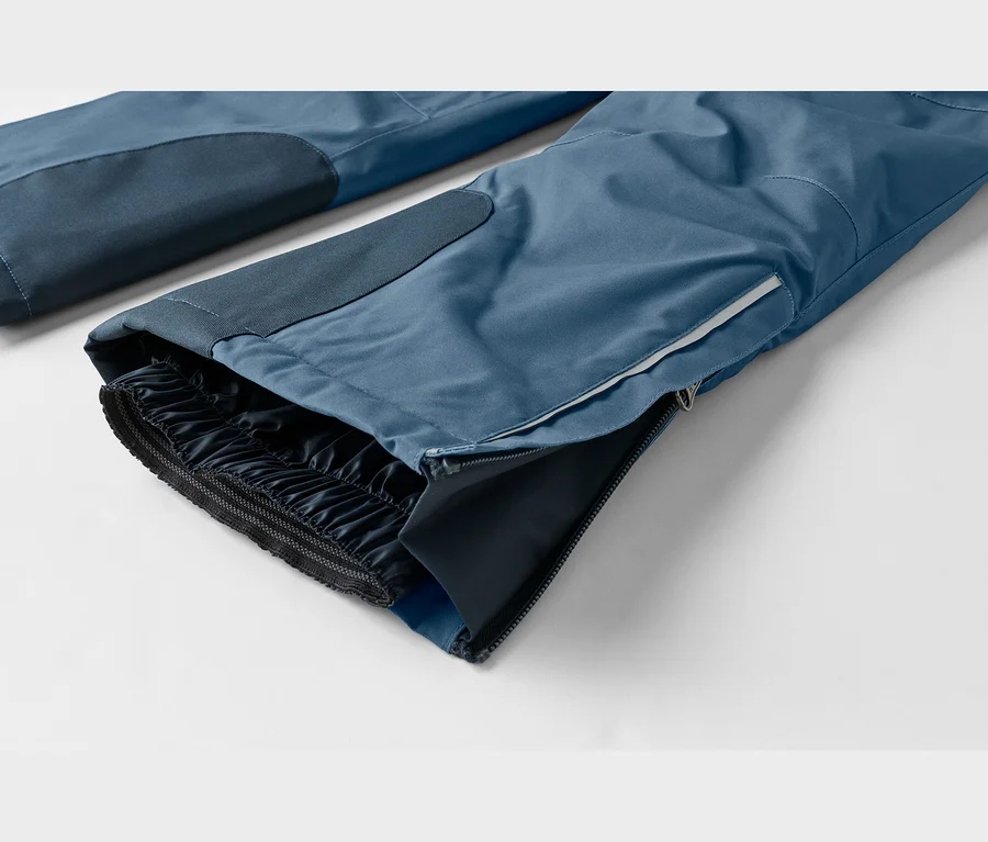 Nahaufnahme einer blauen Funktionshose, die den unteren Beinbereich mit einem teilweise geöffneten Seitenreißverschluss, einem weißen Streifen und einem elastischen dunklen Innenbündchen zeigt.