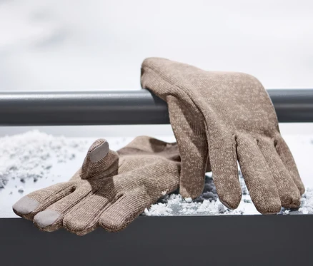 Braune Strickfleece-Handschuhe liegen auf einer verschneiten Oberfläche.
