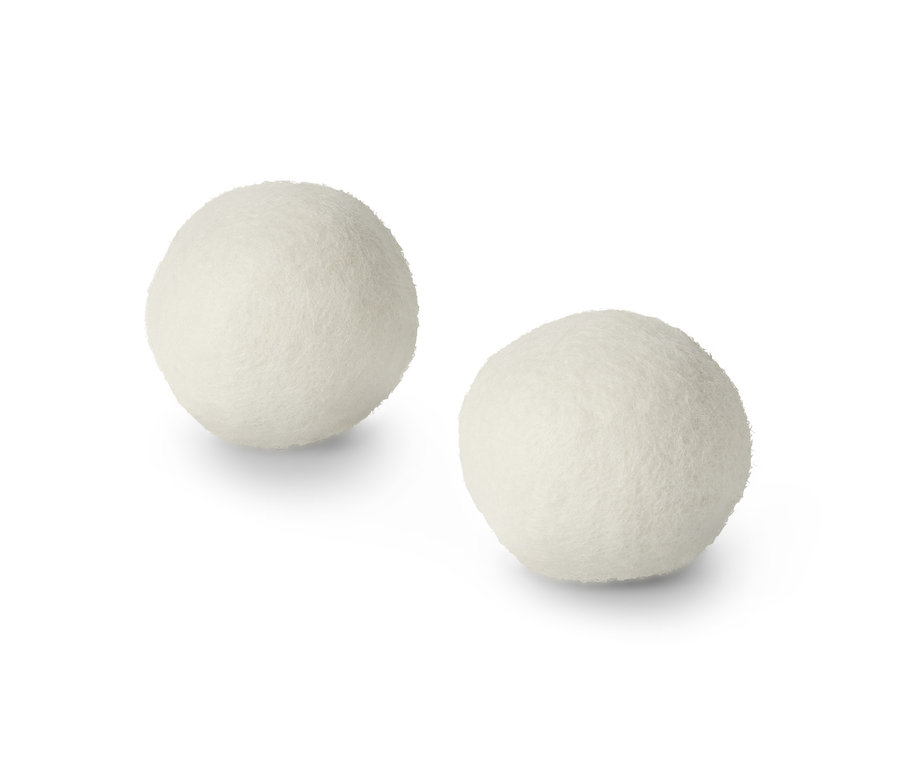 Zwei Trocknerbälle aus Wolle liegen auf einem weißen Untergrund.