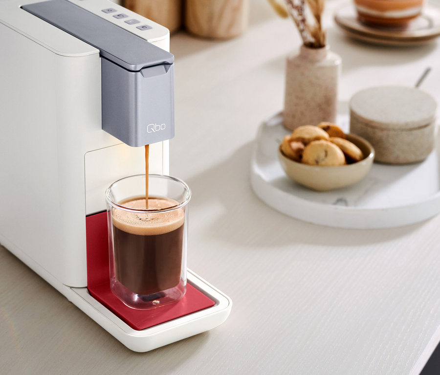 Kaffee läuft aus einer Qbo ESSENTIAL Bright Coral Kaffeemaschine in ein Glas.