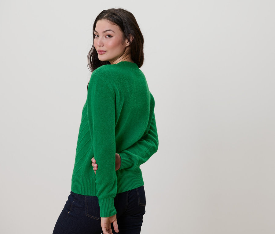 Frau blickt über die Schulter und trägt einen grünen Cardigan mit Strickstruktur.