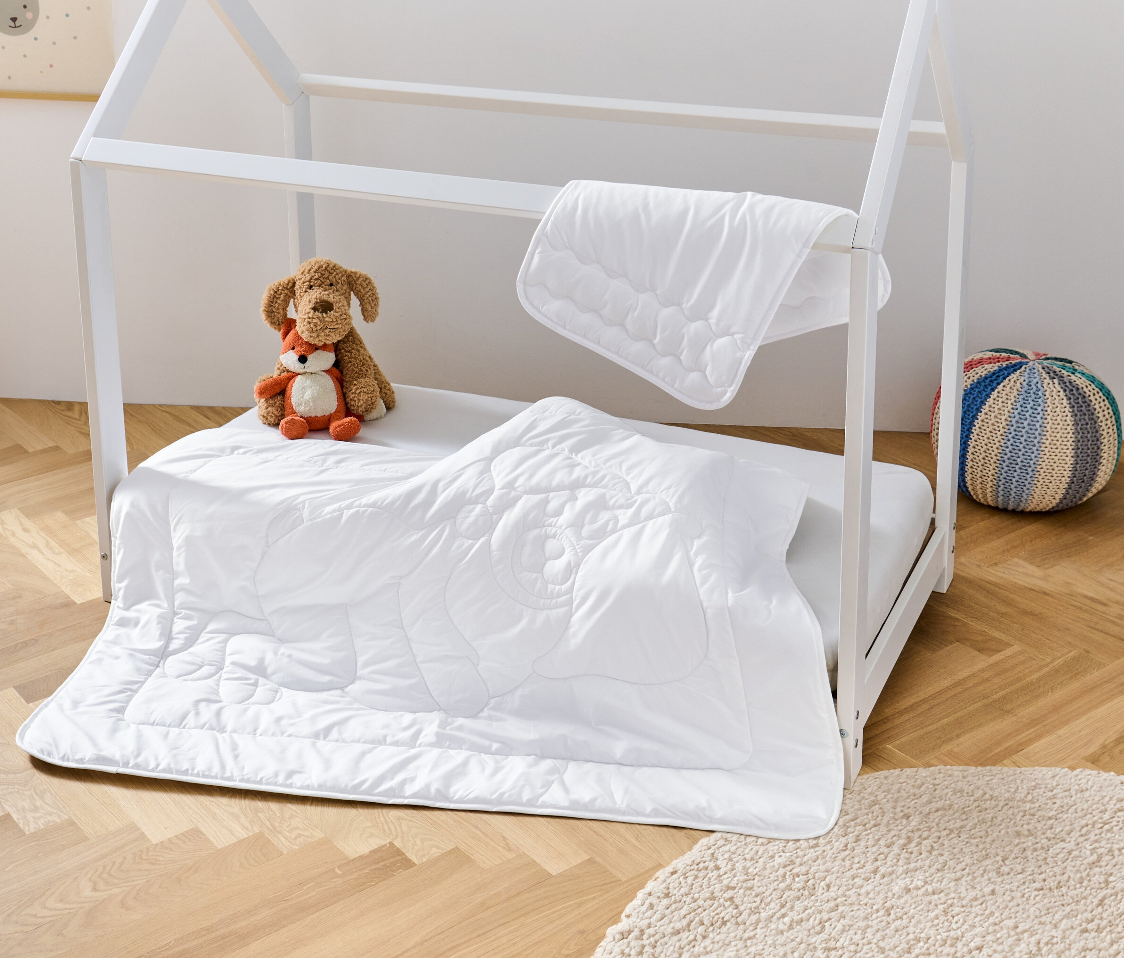 Weißes Kinderbett mit irisette® greenline Kinder-Steppdecke und -Kissen, Stofftieren und Hocker.