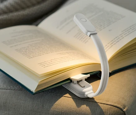 Offenes Buch mit LED-Leseleuchte auf einem grauen Sofa.